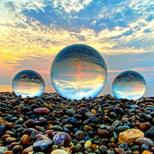 Load image into Gallery viewer, Three crystal balls on a pebble beach with a colorful sunset sky.