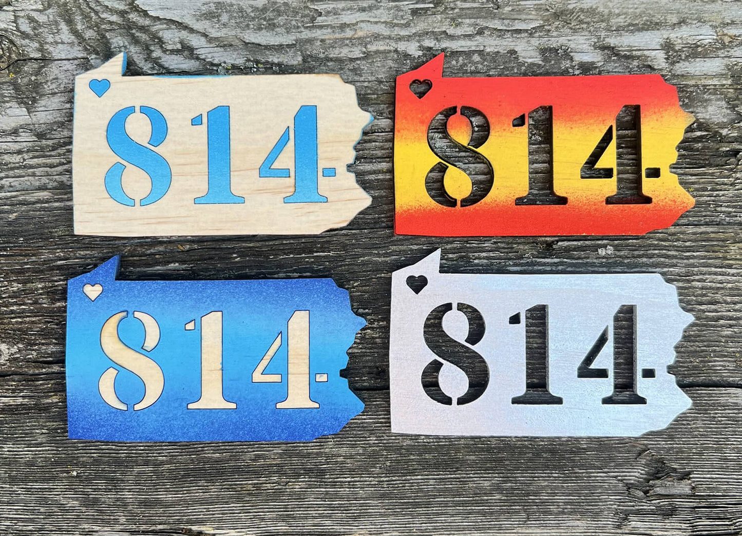 Four different colored wooden magnets in the shape of Pennsylvania with 814 cut of of the middle and a heart cut out of the location of Erie, Pennsylvania 