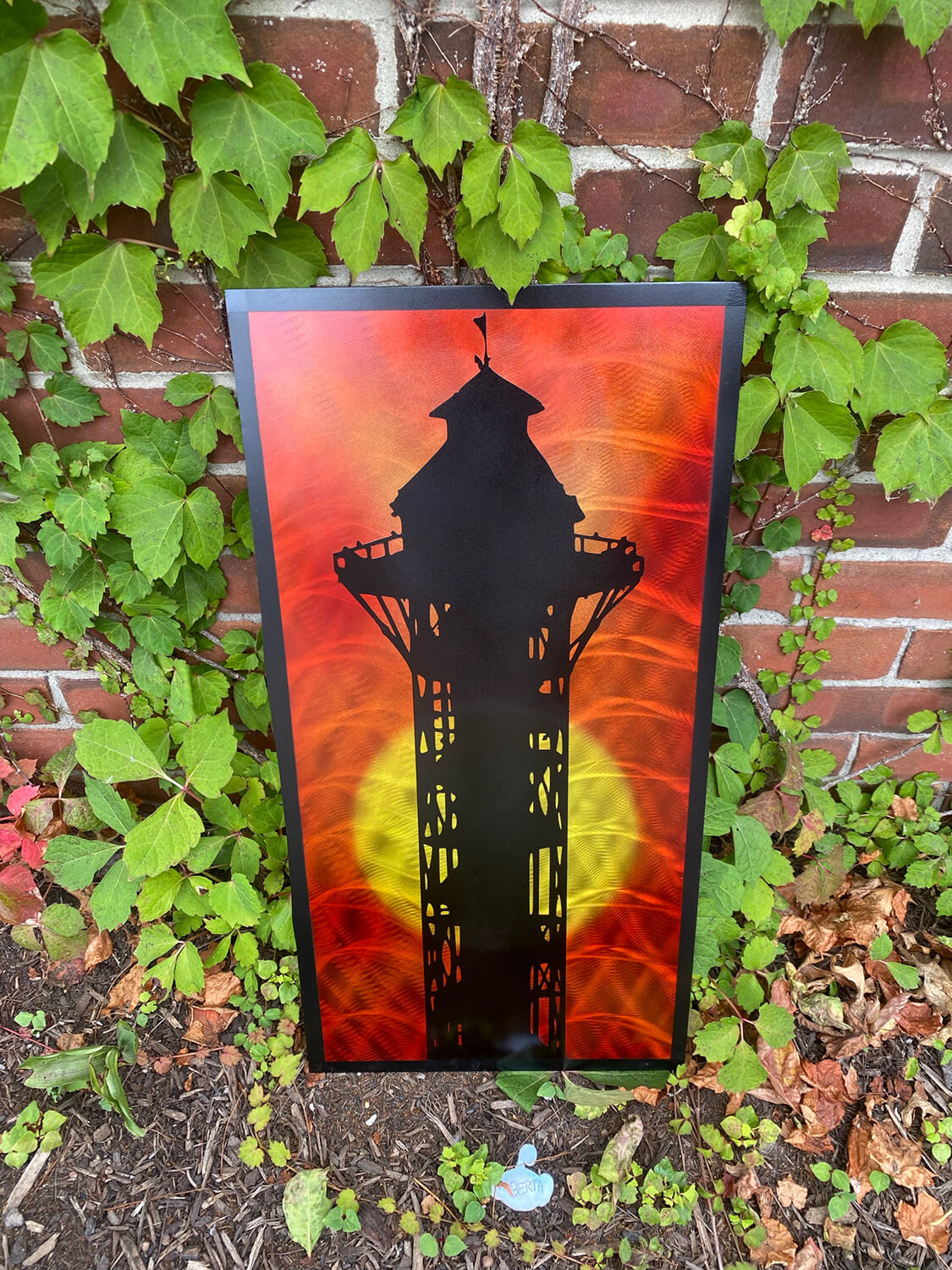 Metal artwork of the silhouette of the bicentennial tower in front of a red and orange sunset with a yellow sun