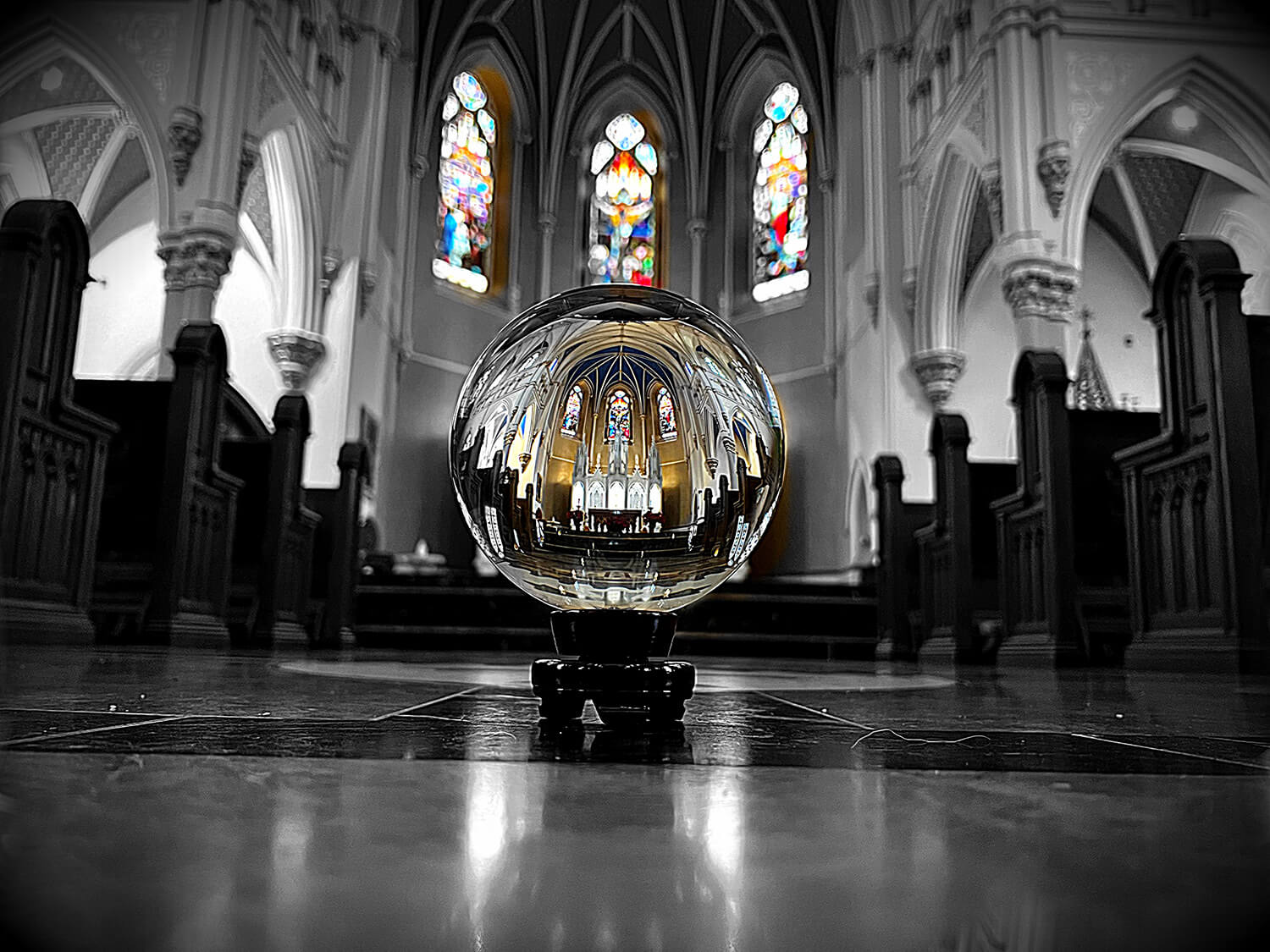 Greyscale photograph of a crystal sphere colorfully reflecting stained glass windows in a cathedral