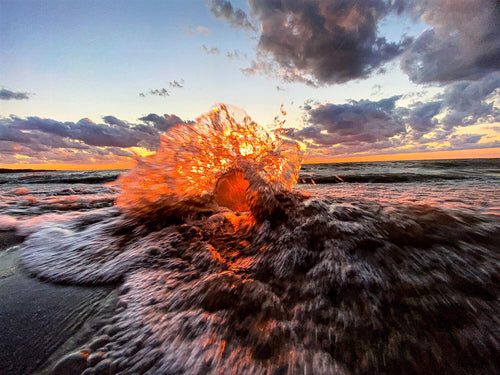 A wave crashing into a crystal ball on a beach with a sunset.