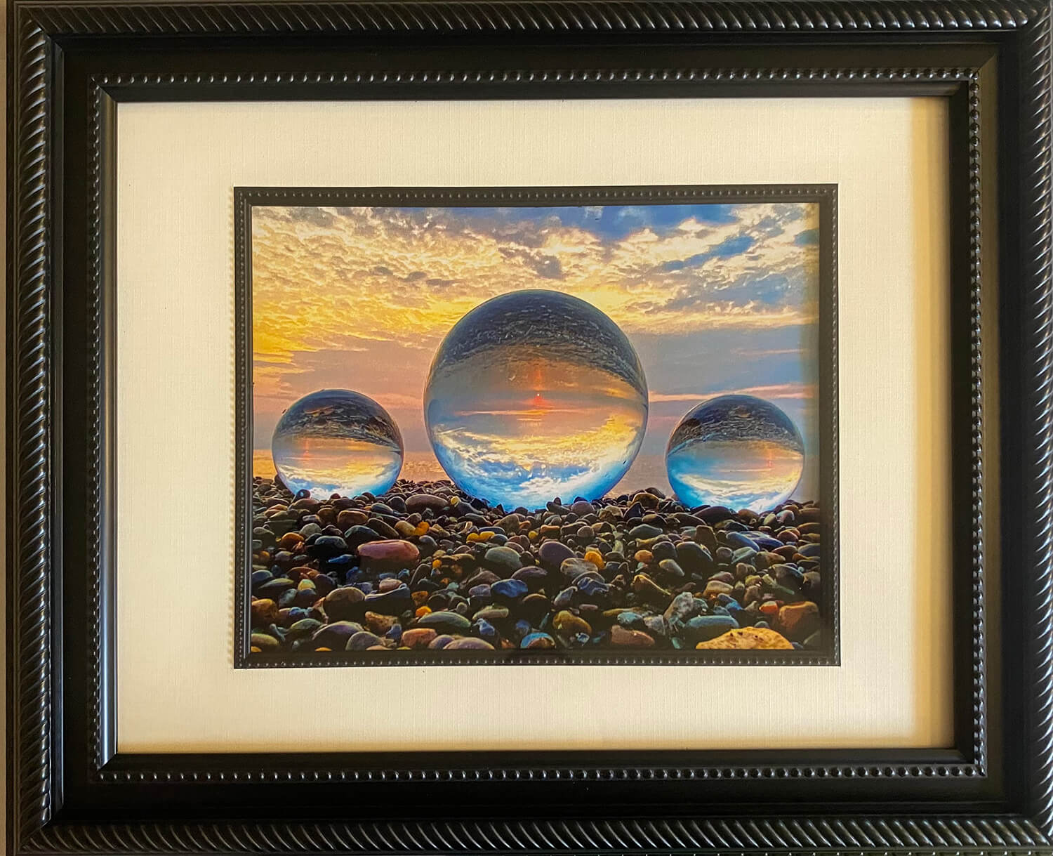 Framed photograph of three crystal balls on a pebble beach with a colorful sunset sky.