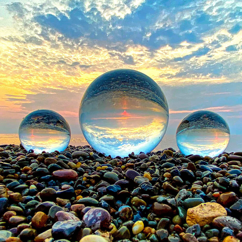 Three crystal balls on a pebble beach with a colorful sunset sky.